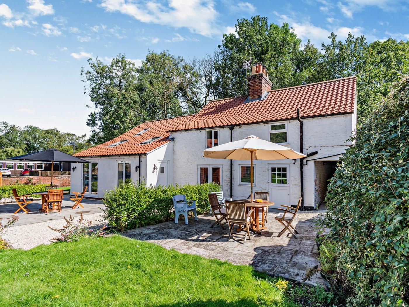 A white house with a red-tiled roof, a patio with outdoor furniture, and a garden.