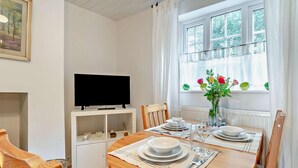A dining area with a wooden table set for two, a television on a white stand, and a window with curtains. - 2 Bed in Driffield (oc-93141) (Langtoft)