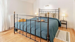 A bedroom with a metal-framed bed, a bedside table with a lamp, a radiator, and a window with curtains. - 2 Bed in Driffield (oc-93141) (Langtoft)
