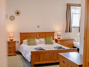 Un dormitorio con una cama de madera, dos mesitas de noche con lámparas, un aparador y una ventana con cortinas.