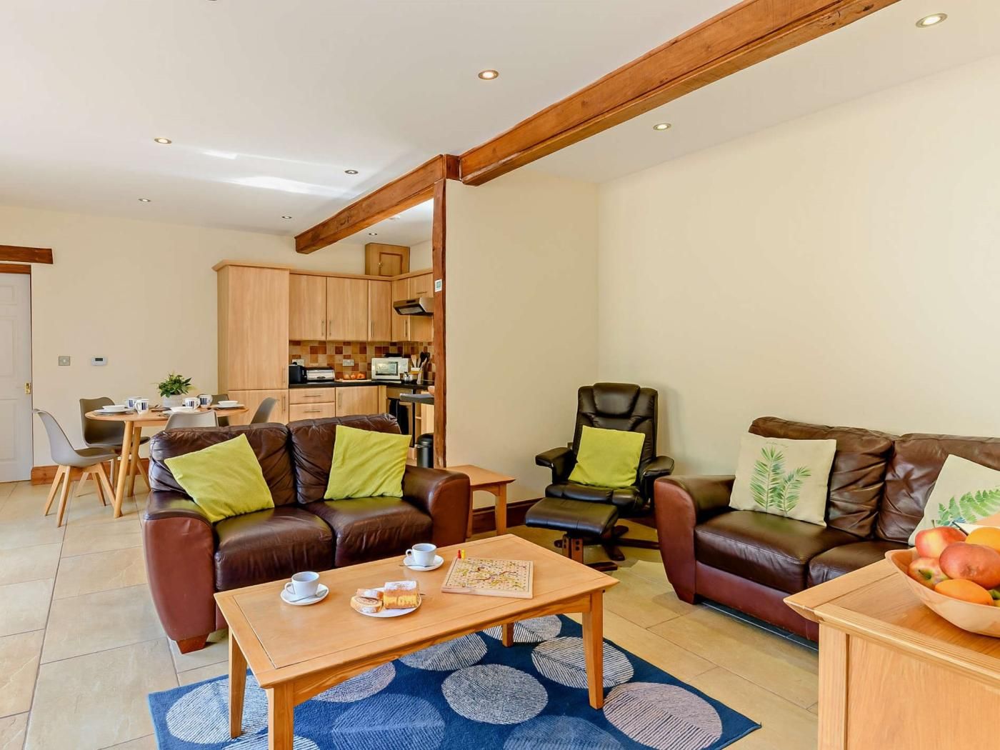 A modern living room with a brown leather sofa, a wooden coffee table, and a dining area with a table and chairs.
