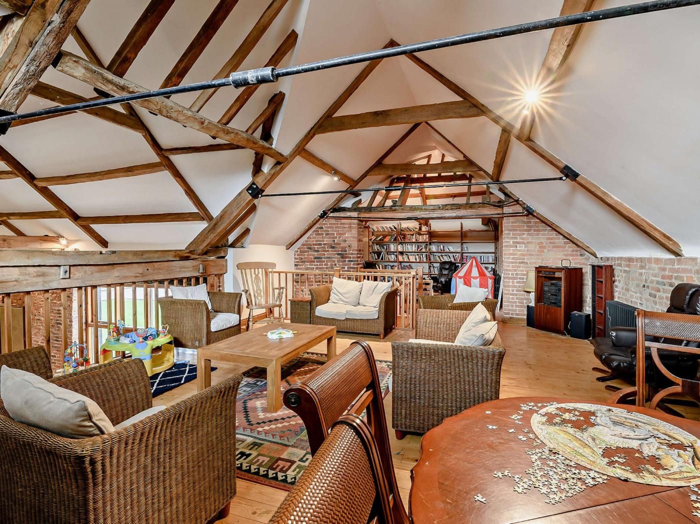A spacious loft with exposed wooden beams, a brick wall, and a cozy seating area with wicker furniture.