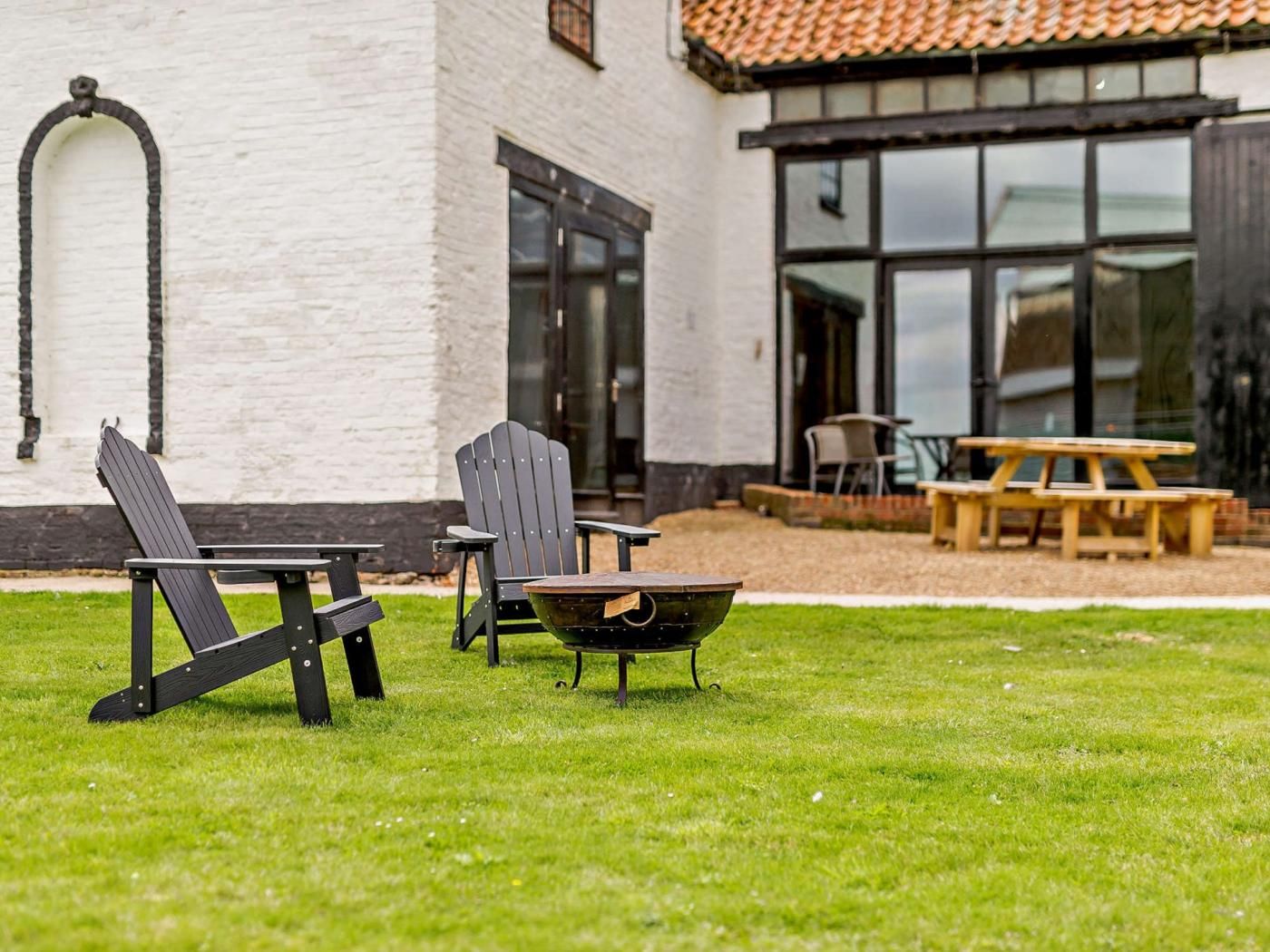 A patio area with two Adirondack chairs, a wooden table, and a fire pit.