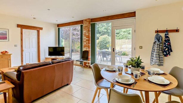 Ein modernes Wohnzimmer mit Sofa, Fernseher und Essbereich mit Tisch für zwei Personen.