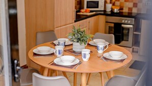 Ein Essbereich mit einem runden Tisch, gedeckt für vier Personen, umgeben von Stühlen. Im Hintergrund befinden sich eine Mikrowelle und ein Backofen.