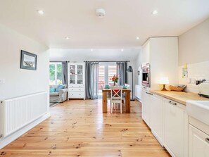 A modern kitchen with white cabinets, a dining area with a wooden table, and a view of the outdoors through large windows. - 2 Bed in Driffield (oc-93140) (Langtoft)