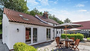 A small white house with a tiled roof, a patio with a table and chairs, and a large umbrella. - 2 Bed in Driffield (oc-93140) (Langtoft)