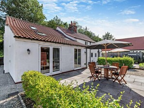 A small white house with a tiled roof, a patio with a table and chairs, and a large umbrella. - 2 Bed in Driffield (oc-93140) (Langtoft)