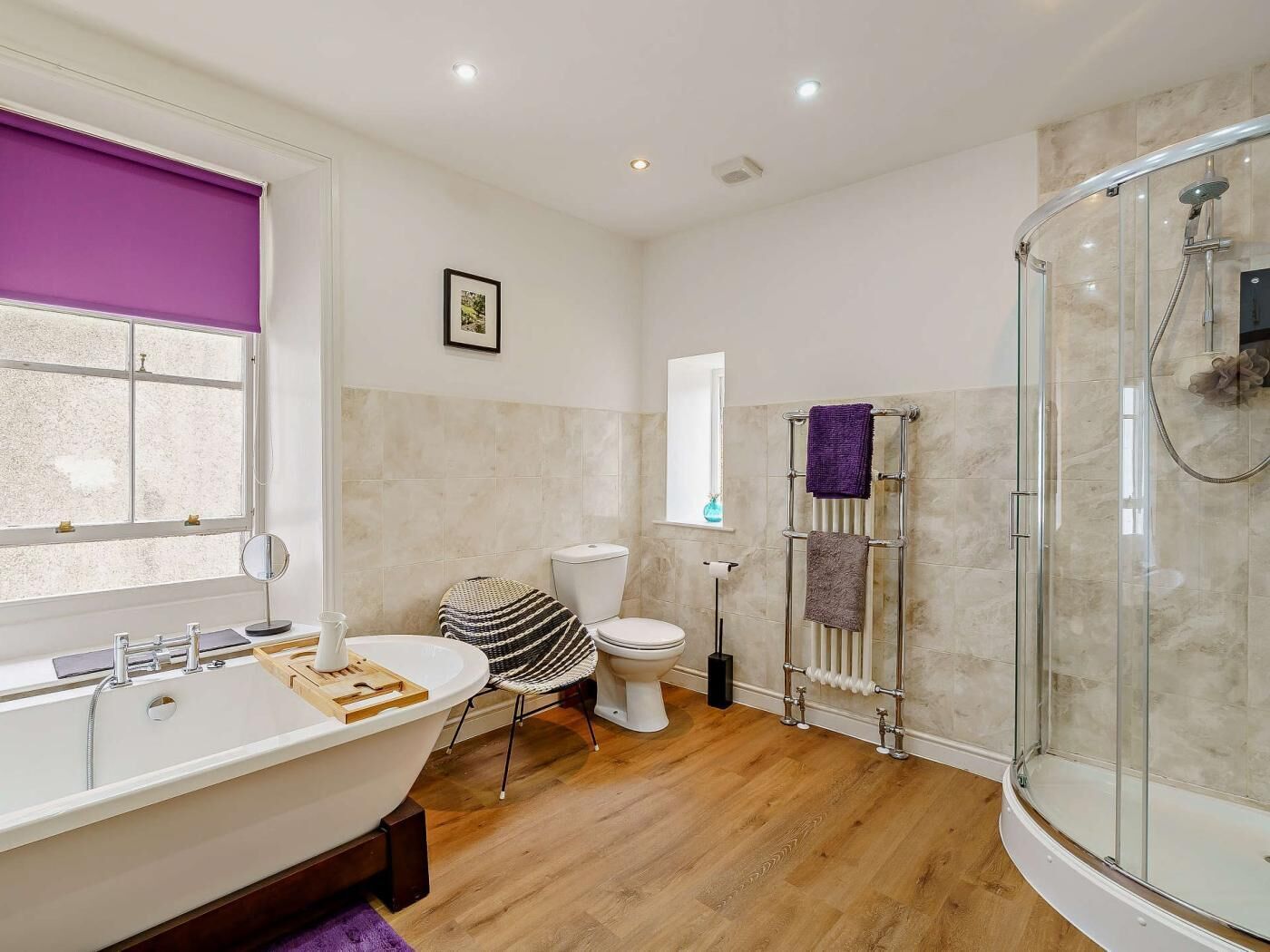 Une salle de bain moderne avec une baignoire sur pieds, une douche à parois de verre, des toilettes et une fenêtre avec un store violet.