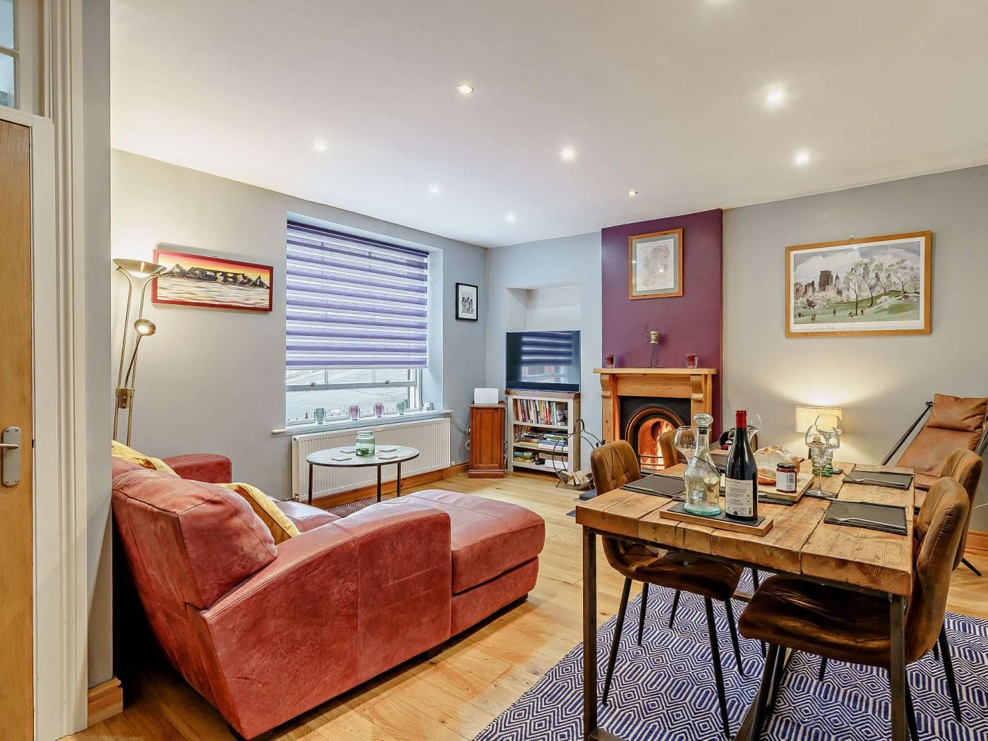 A living room with a red sofa, a dining table with chairs, a fireplace, and a bookshelf.