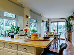 Una cocina con encimera de madera, cafetera, hogaza de pan y comedor con mesa y sillas.