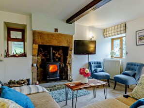A cozy living room with a stone fireplace, a television mounted on the wall, and comfortable seating. - 3 Bed in Stoke-on-trent (oc-92799) (Ipstones)