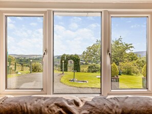 Ein Zimmer mit großem Fenster und Blick auf eine grüne Landschaft mit Bäumen und einer Straße.