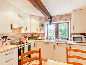A kitchen with white cabinets, a wooden ceiling beam, a window with a view of greenery, and a microwave on the counter. - 2 Bed in Skipton (oc-92898) (Otterburn)