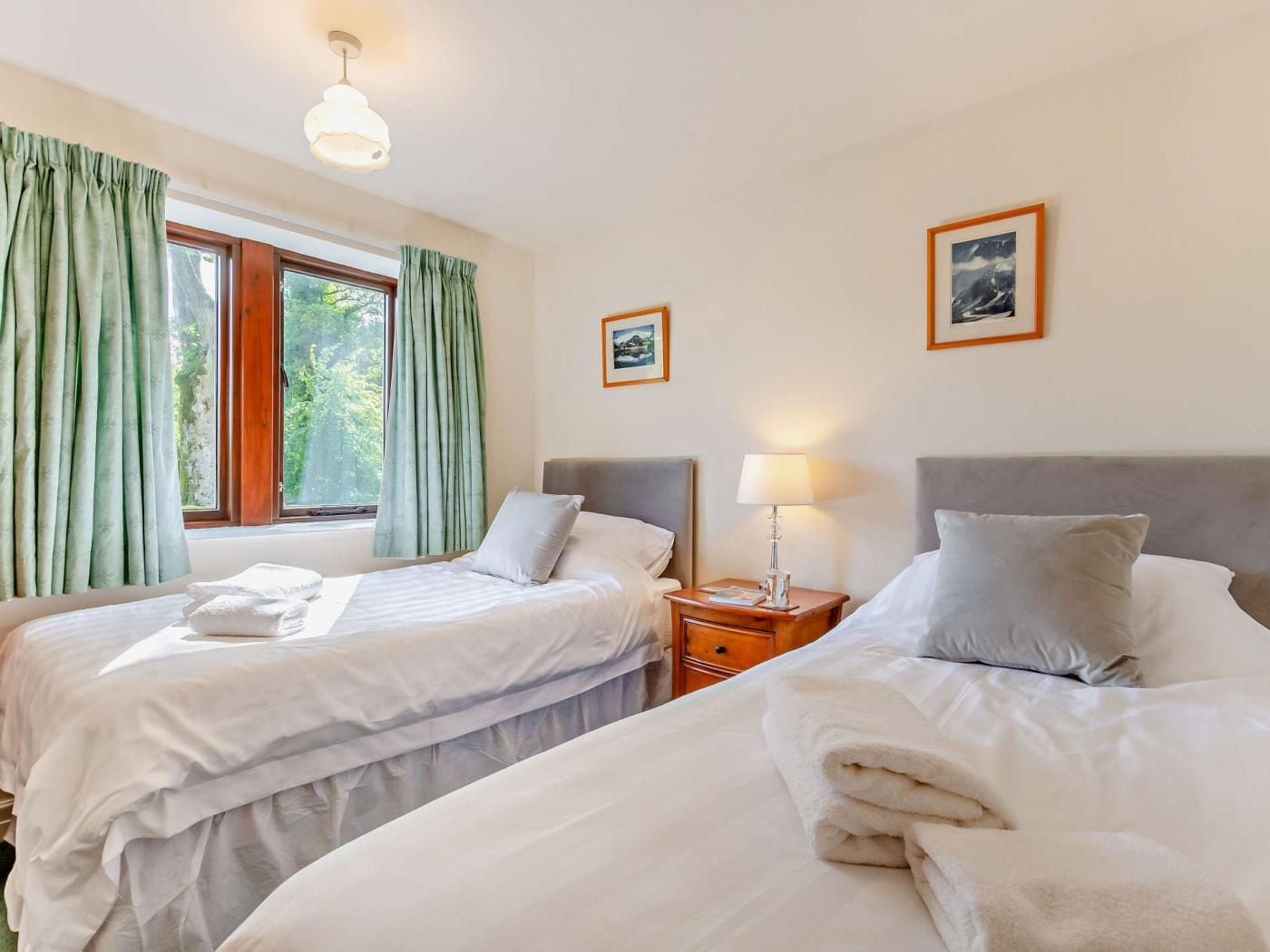 A hotel room with two beds, a nightstand with a lamp, and a window with curtains.
