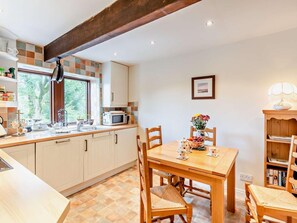 A kitchen with a dining table, chairs, a microwave, and a window with a view of trees. - 2 Bed in Skipton (oc-92898) (Otterburn)