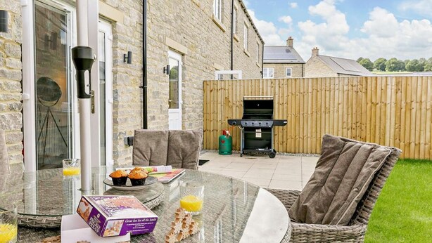 Une terrasse dotée de meubles en osier, d’une table en verre et d’un barbecue.