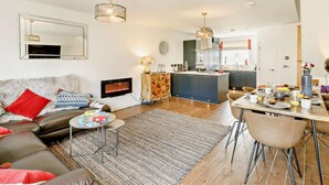 Un salon moderne avec un canapé, une table basse et un téléviseur. Il y a une cuisine avec un coin repas et un grand miroir.