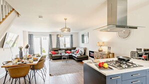 Une cuisine moderne équipée d’une cuisinière à gaz, un coin repas avec des chaises et une table, un canapé et un escalier.