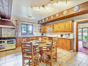 A kitchen with wooden cabinets, a dining table with chairs, a stove, and a window with curtains. - 3 Bed in Weymouth (oc-92902) (Osmington)