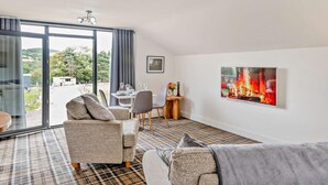 A modern living room with a dining area, large windows, and a fireplace painting. - 2 Bed in Sheffield (oc-92978) (Upper Midhope)