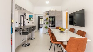 Een moderne keuken met een eethoek, met een witte tafel, bruine stoelen en een aan de muur bevestigde televisie.