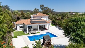 A two-story house with a swimming pool, surrounded by greenery and hills. - Luxury Family Villa | Pool, Mini Golf & Playhouse | Sotogrande Costa (Cádiz)