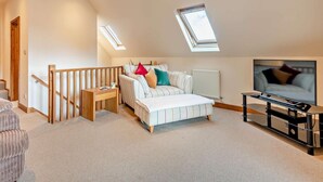 Ein Schlafzimmer mit geneigter Decke, einem Bett, einem Fernseher und einem Fenster.