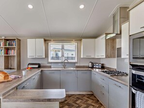 A compact kitchen with grey cabinets, a built-in oven, a window with blinds, and a herringbone wood floor.