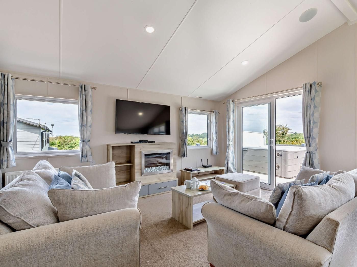 A modern living room with a flat-screen TV, a fireplace, and a balcony with curtains.