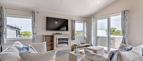A modern living room with a flat-screen TV, a fireplace, and a balcony with curtains.