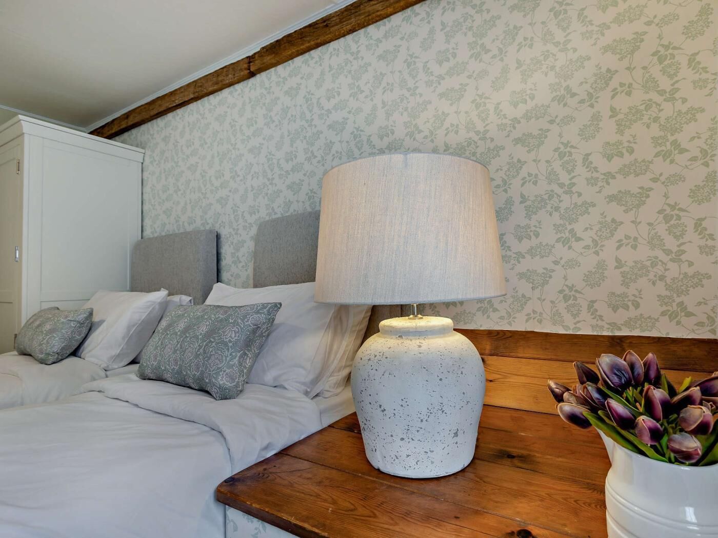 A bedroom with a bed, a nightstand, a lamp, and a vase with flowers.