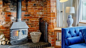 Una habitación con chimenea de ladrillo, estufa moderna, cesto de mimbre, sofá azul y una lámpara.