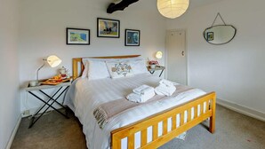 Un dormitorio con una cama de madera, una mesita de noche con lámpara, un espejo en la pared y tres cuadros enmarcados.