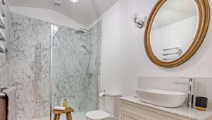Un bagno con doccia in marmo, un water, un lavandino con un grande specchio e uno sgabello di legno.
