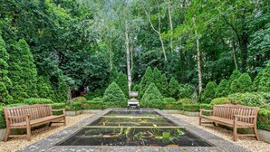 Un giardino con un elemento d'acqua rettangolare, due panchine in legno e un muro in pietra.