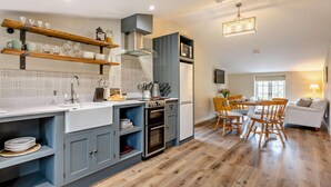 Una cucina moderna con forno integrato, una zona pranzo con sedie di legno e un soggiorno con divano.