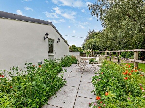 A white building with a sloped roof, a paved patio with a table and chairs, and a wooden fence. - 2 Bed in Barnstaple (oc-93023) (Chapelton)
