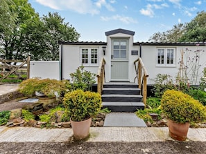 A two-story building with a front entrance, a staircase, and a garden with potted plants. - 2 Bed in Barnstaple (oc-93023) (Chapelton)