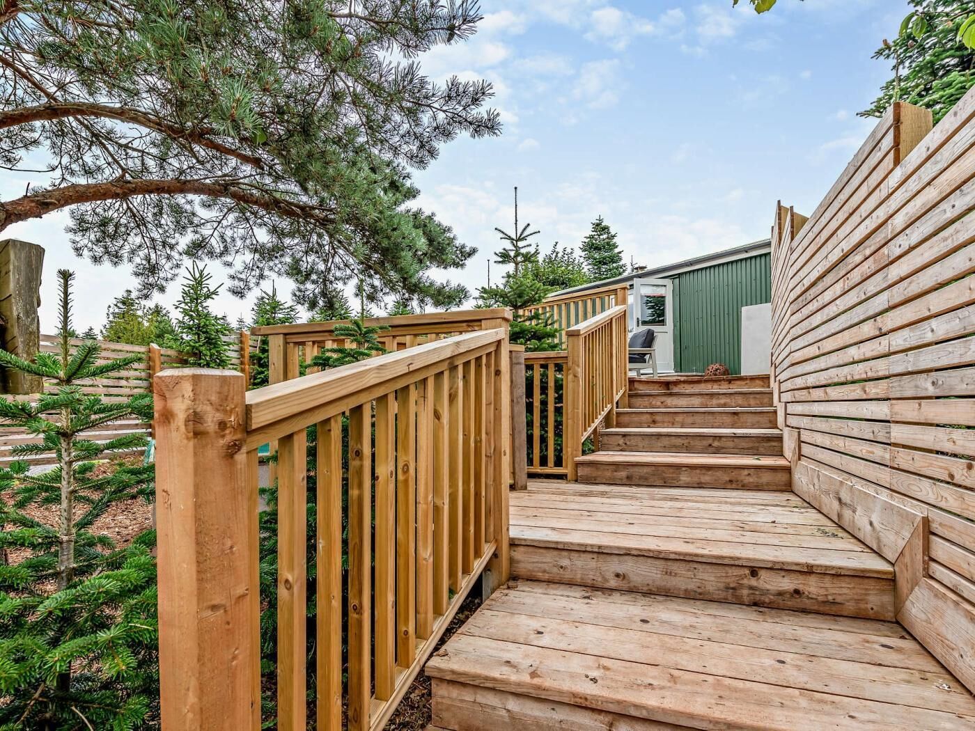 A wooden staircase leading to a deck with a railing, surrounded by trees.