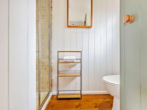 A bathroom with a wooden floor, a white toilet, a glass shower enclosure, and a metal shelf with a towel. - 1 Bed in Paignton (oc-93063) (Marldon)