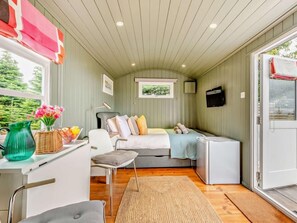 A compact room with a bed, a desk, a chair, a small table, a TV, and a window with a view of greenery. - 1 Bed in Paignton (oc-93063) (Marldon)