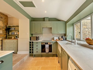 A kitchen with green cabinets, a stone wall, and a window with a view. - 2 Bed in Bridport (oc-93076) (Burton Bradstock)