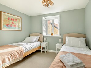 A bedroom with two beds, a window with blinds, a bedside table with a lamp, and a framed picture on the wall. - 2 Bed in Bridport (oc-93076) (Burton Bradstock)