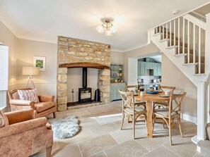 A cozy living room with a stone fireplace, a dining area with wooden chairs, and a staircase leading to an upper level. - 2 Bed in Bridport (oc-93076) (Burton Bradstock)