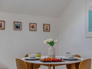 A dining area with a table set for two, a vase of white flowers, and a croissant on the table. - 1 Bed in Paignton (oc-93061) (Marldon)