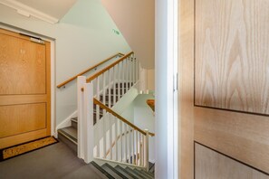 Eine Holztür mit Hausnummer, eine weiße Treppe mit hölzernem Geländer und ein grünes Ausgangsschild.