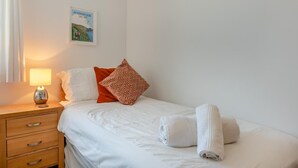 Een hotelkamer met een bed, nachtkastje met lamp, een kussen, handdoek en een wanddecoratie.