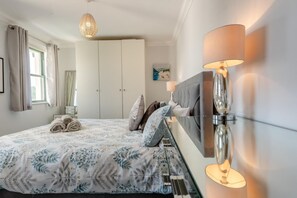 Ein Schlafzimmer mit Bett, Nachttisch, Lampe, Kleiderschrank und einem Fenster mit Vorhängen.