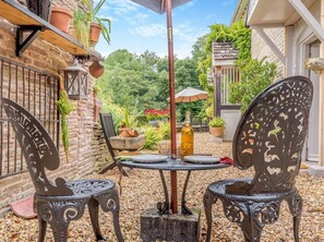 Un patio al aire libre con dos sillas de metal, una mesa y una botella de vino.